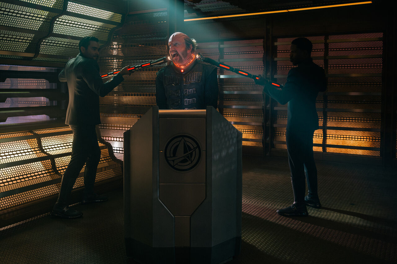 한 외계인 남자가 다른 두 외계인 남자에 의해 제지당하고 있습니다.