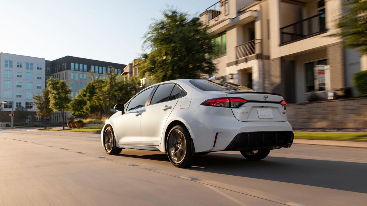 街中を走行する白い 2025 トヨタ カローラ XSE のダイナミックなリア 3/4 ショット。