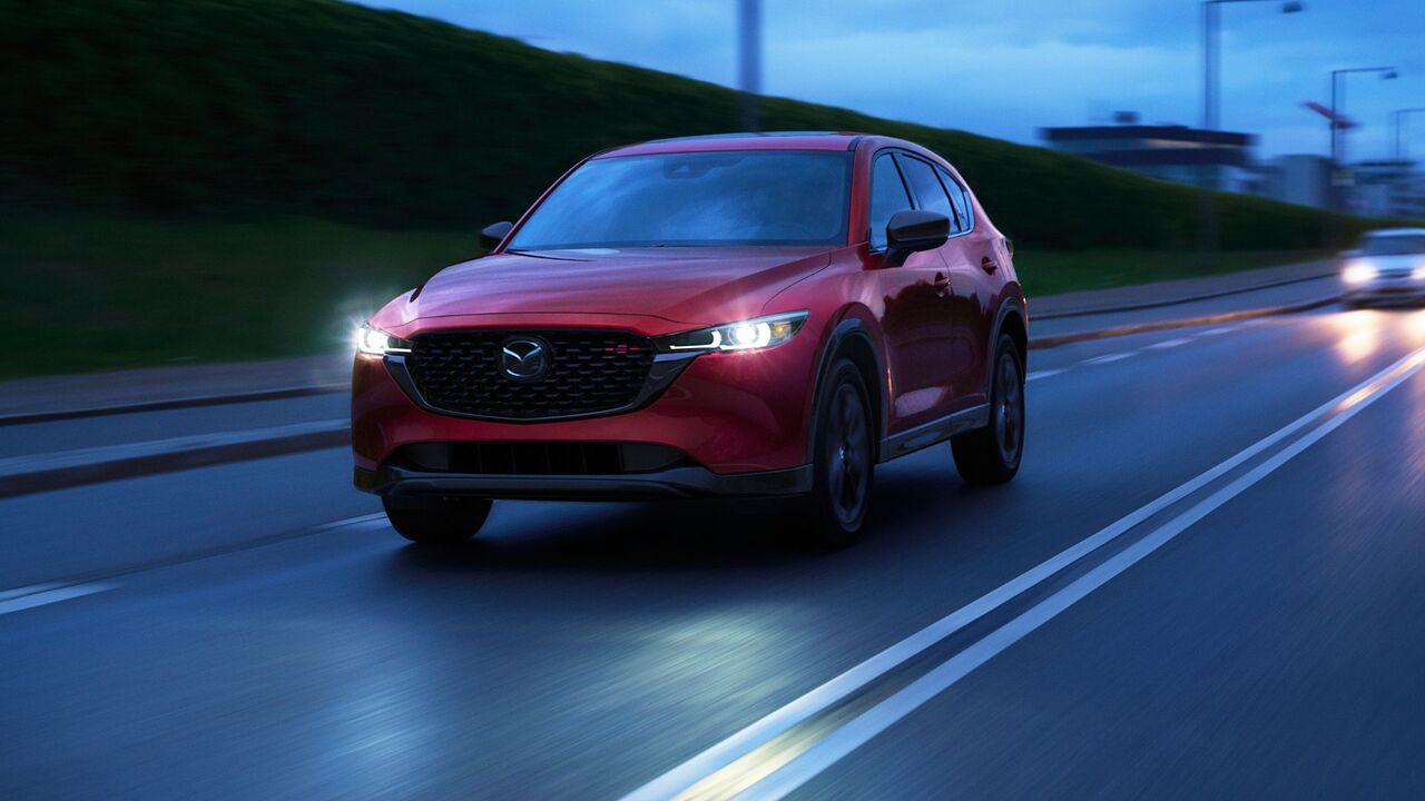 夜間に街中を走行する赤い 2025 型マツダ CX-5 の正面からの 4 分の 3 のビュー。