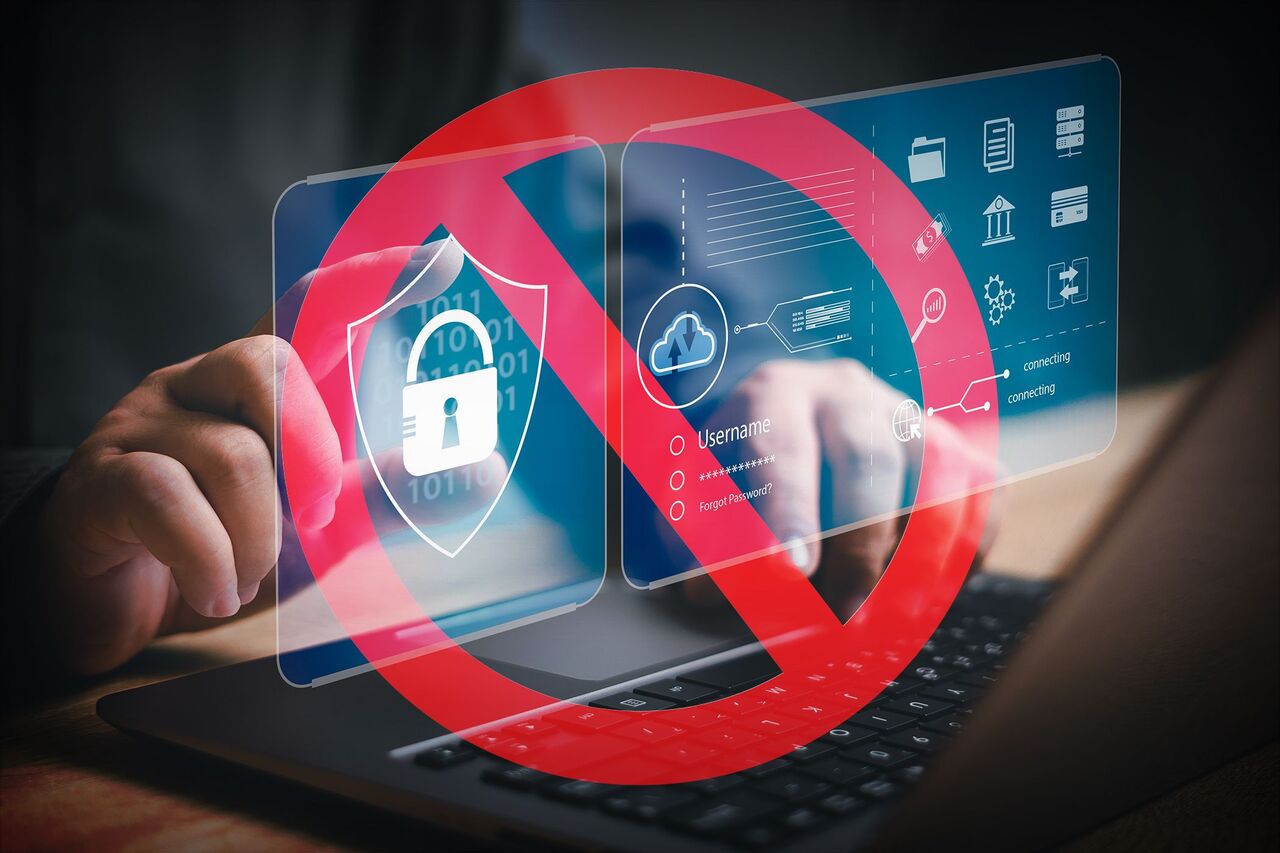 デジタル アクセスの制限を示す、セキュリティ アイコンの上に赤い禁止標識が表示されたラップトップで入力する手。