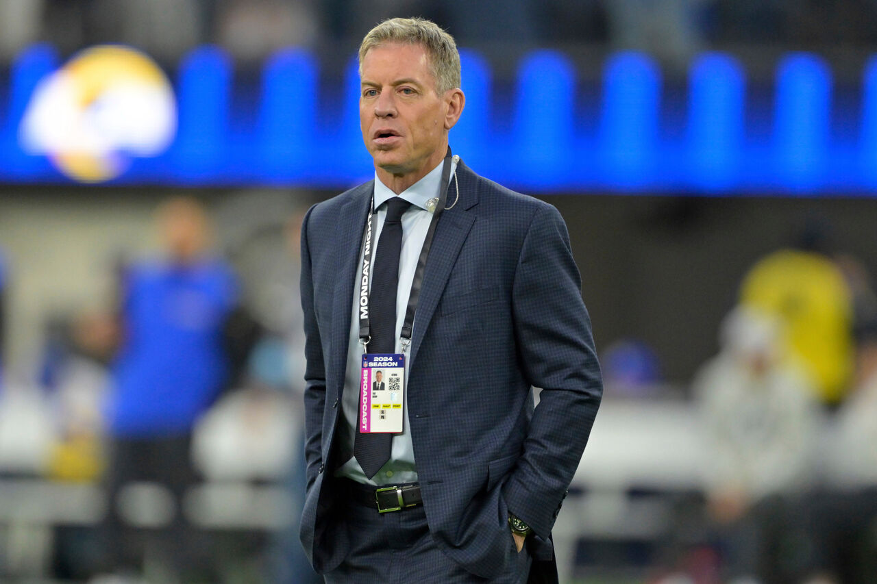 ID 배지가 달린 양복을 입고 축구장에 서 있는 Troy Aikman.