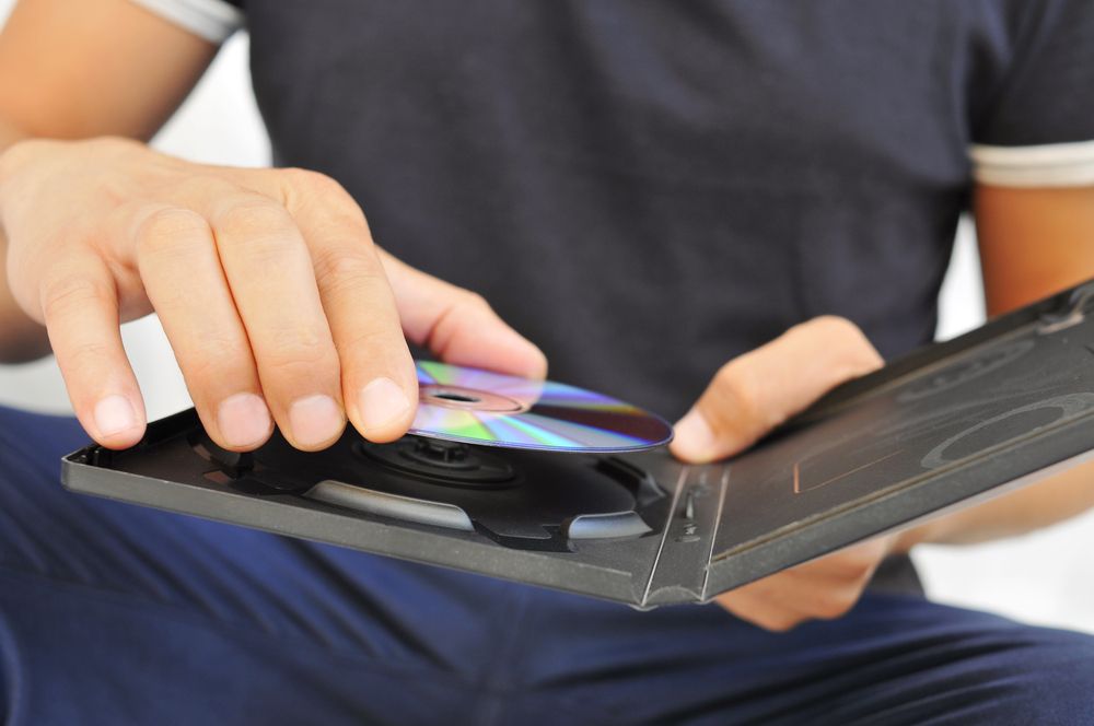 DVD または CD をケースから取り出す若い男性の接写。