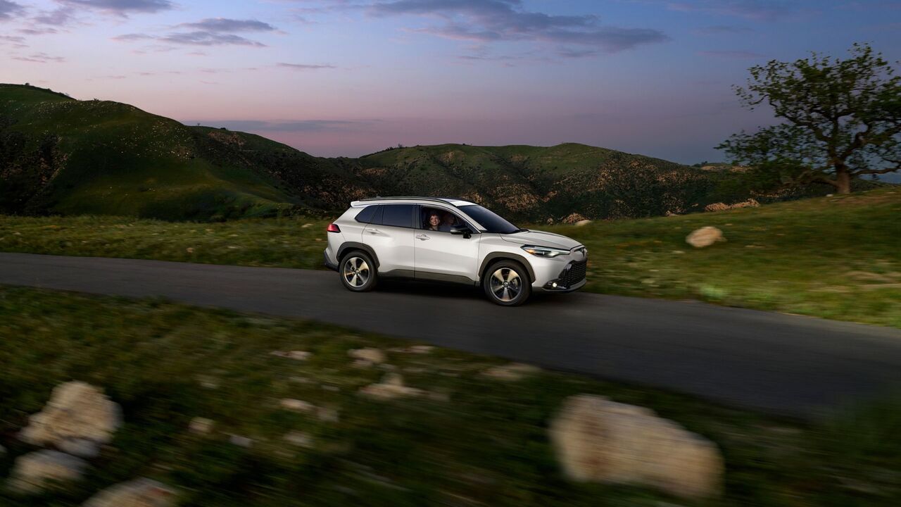 白い 2025 トヨタ カローラ クロス ハイブリッド XSE のダイナミックな側面ショット。