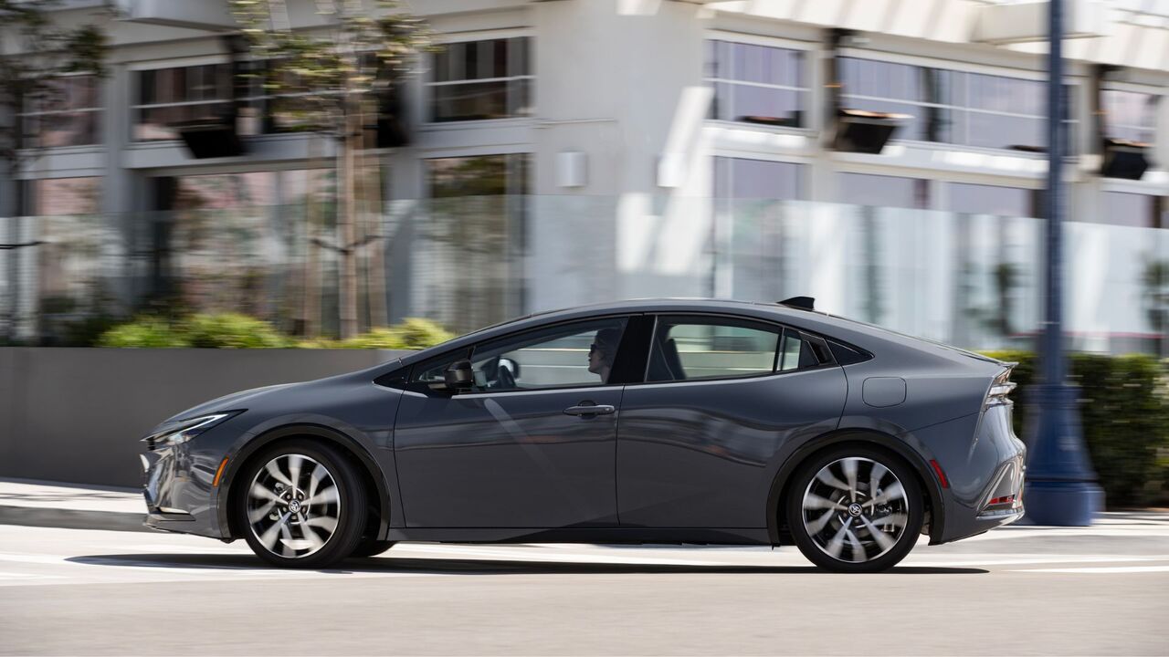 街中で走行するグレーの 2025 トヨタ プリウス PHEV XSE プレミアムのダイナミックな横顔のショット。