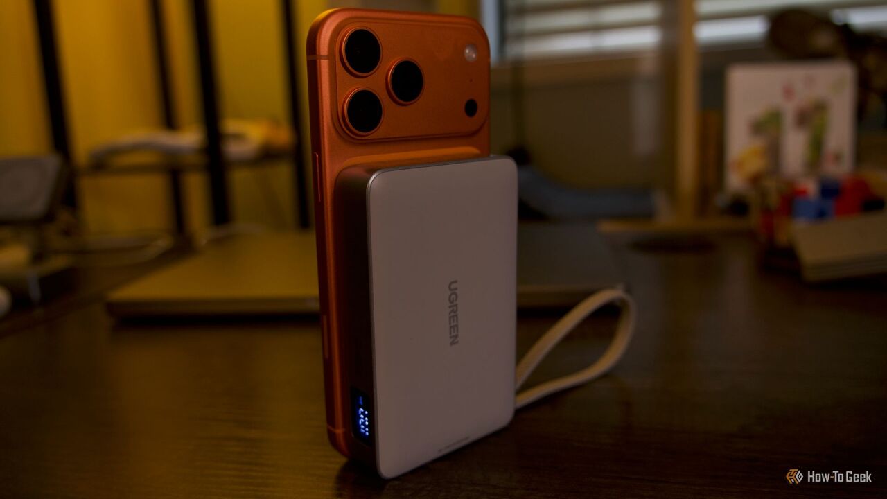 Ugreen MagFlow 10000mAh 25W パワーバンクは、テーブルの上に直立したオレンジ色の iPhone 17 Pro Max に接続されています。