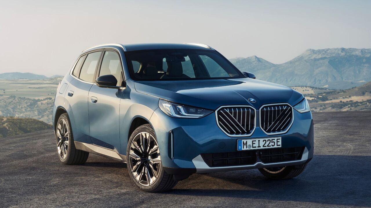 山を背景にした青い 2025 BMW X3 30 xDrive のフロント 3/4 ショット。