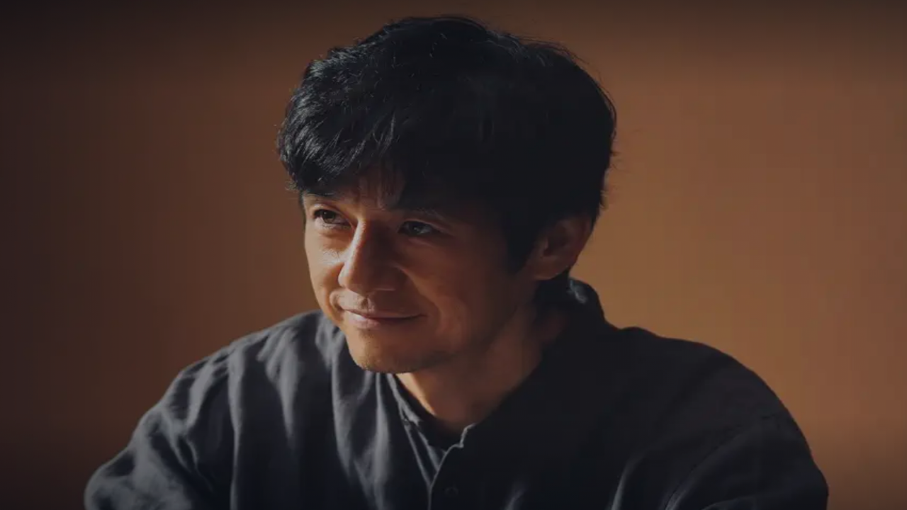 『人間標本』の西島秀俊がグレーのシャツを着て微笑んでいるスクリーンショット。