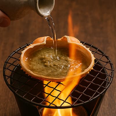 かにの甲羅にカニ味噌をのせて日本酒を注ぎ直火で炙る